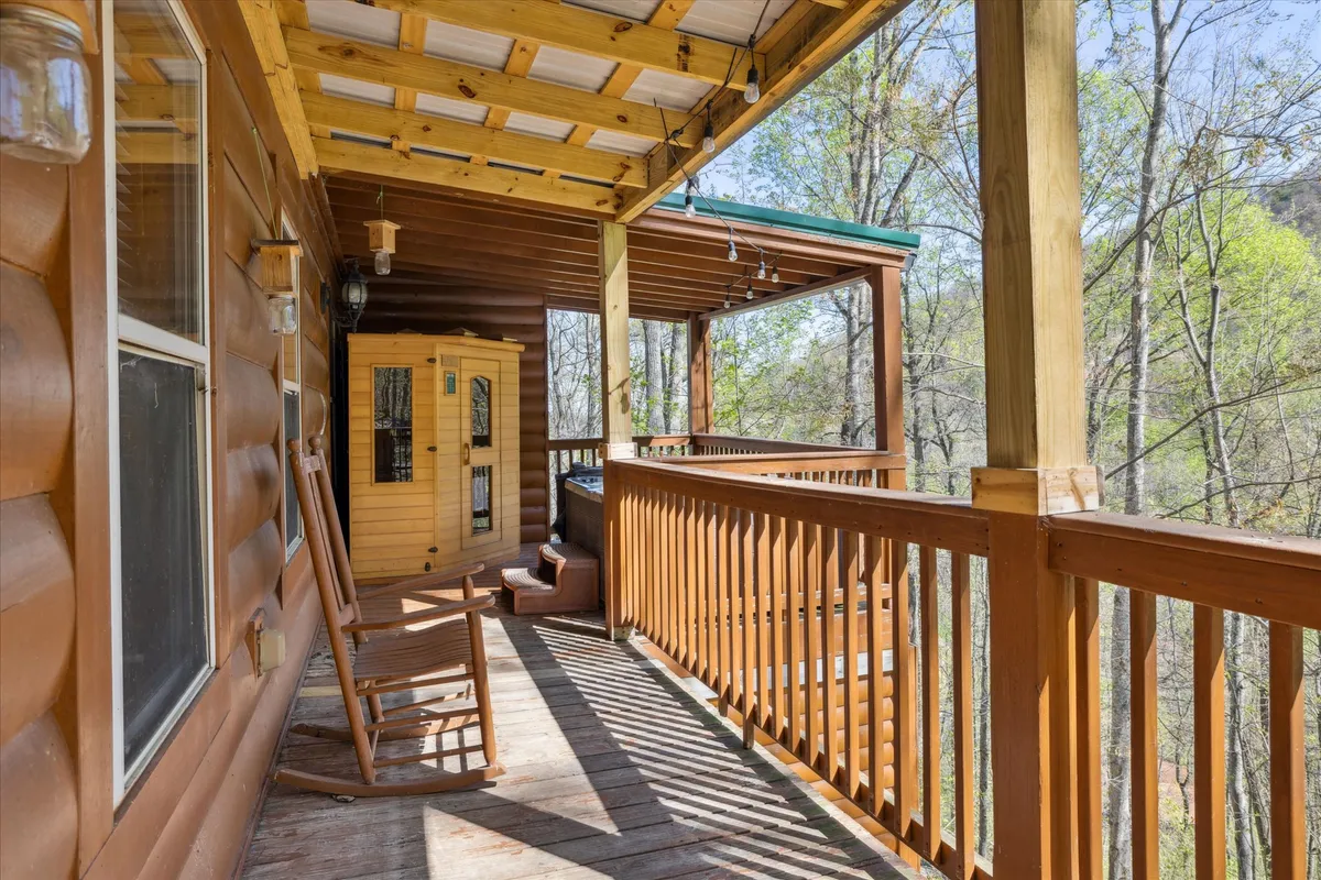 This exterior image shows a rustic sauna beside a rocking chair on a wooden porch, with trees creating a tranquil, private setting. The inviting sauna is the focal point, offering a glimpse of the wellness amenities available.