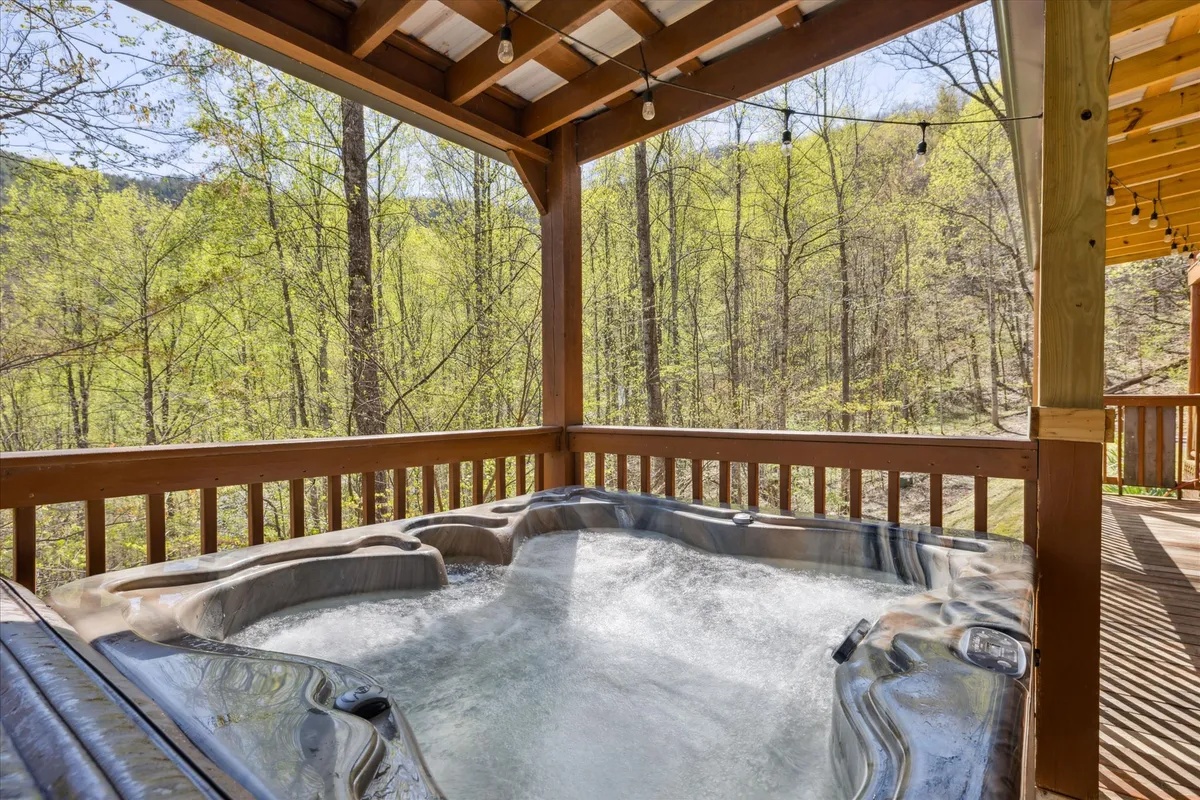 A serene view of the bubbling hot tub nestled on a wooden deck, surrounded by lush trees. The tranquil setting encourages relaxation, reflecting the peaceful seclusion of the cabin’s outdoor living spaces.
