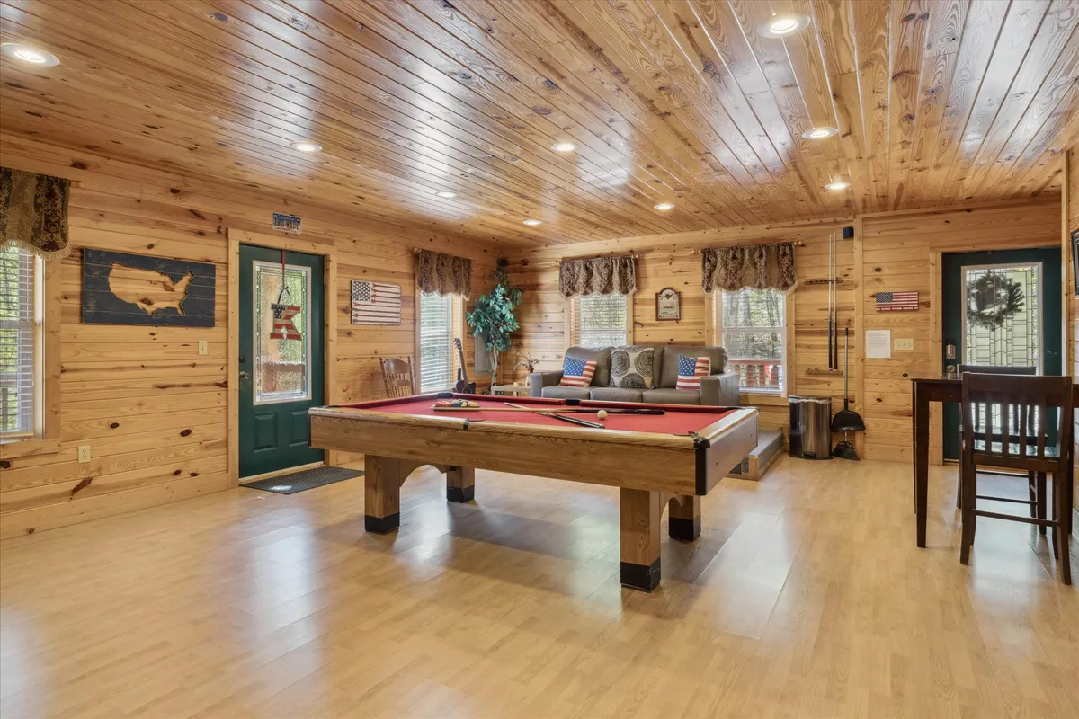 A vibrant game room scene with a full-size pool table, comfortable sofa seating, and decorative wooden wall art. The mood is friendly and relaxed, with guests socializing, enjoying drinks, and engaging in friendly competition, perfectly reflecting the fun-filled entertainment highlighted in the section.