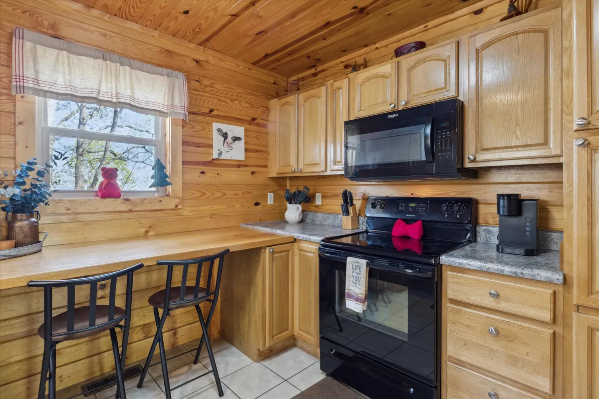 The image spotlights a kitchen with wooden cabinets, sleek black appliances, and a breakfast bar set for casual dining. Decorative touches and ample counter space further enhance its inviting, functional vibe.