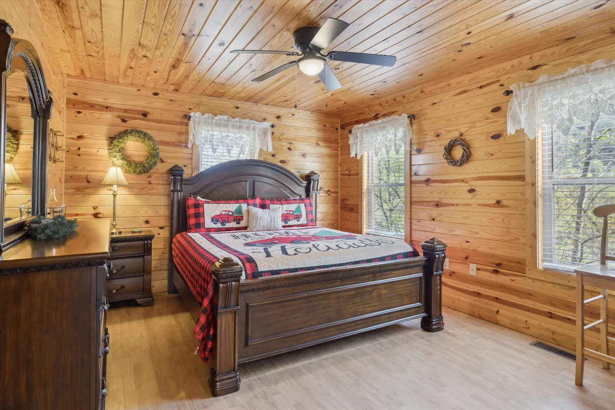 This image features a king bedroom with a sturdy wooden bed frame and inviting plaid bedding. The room is bathed in natural light from a window that offers serene woodland views. The decor is simple yet warm, creating a peaceful retreat ideal for restful sleep.