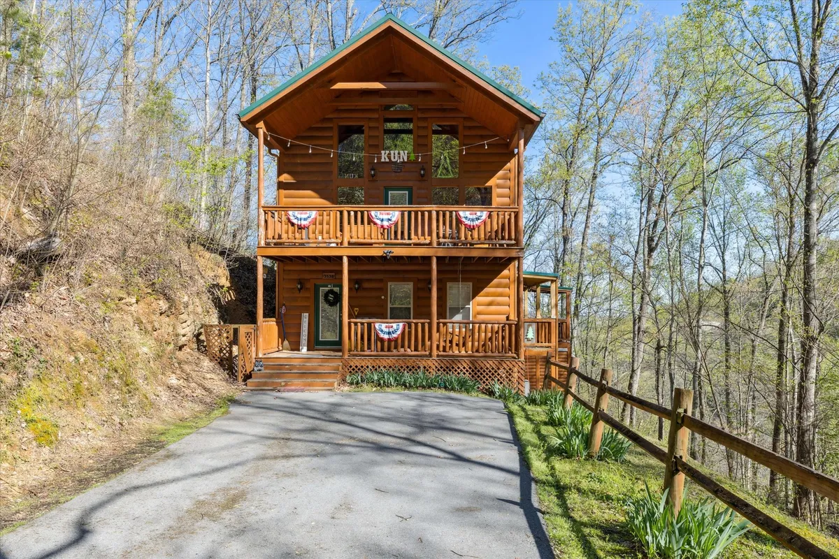 This image features the log cabin’s front porch set against a backdrop of lush trees. Decorative banners and classic railings frame the inviting entry, while the wide porch suggests a space where families can gather to enjoy the outdoors. The natural setting is emphasized by the surrounding greenery, hinting at tranquil mornings and evenings spent close to nature.