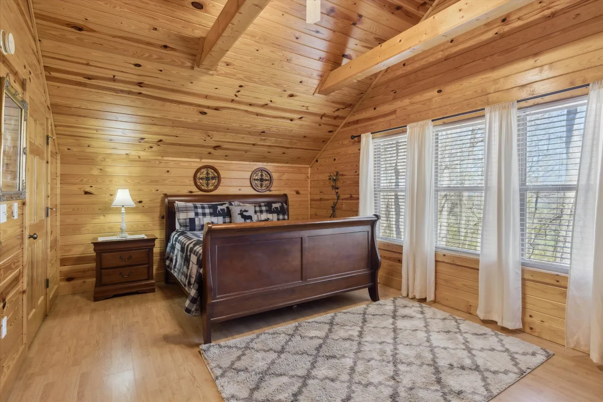 A king bedroom with rustic wooden furnishings, plaid bedding, soft lighting from a bedside lamp, and large curtained windows framing the outdoors. The room exudes comfort and tranquility, perfect for unwinding after a day exploring.