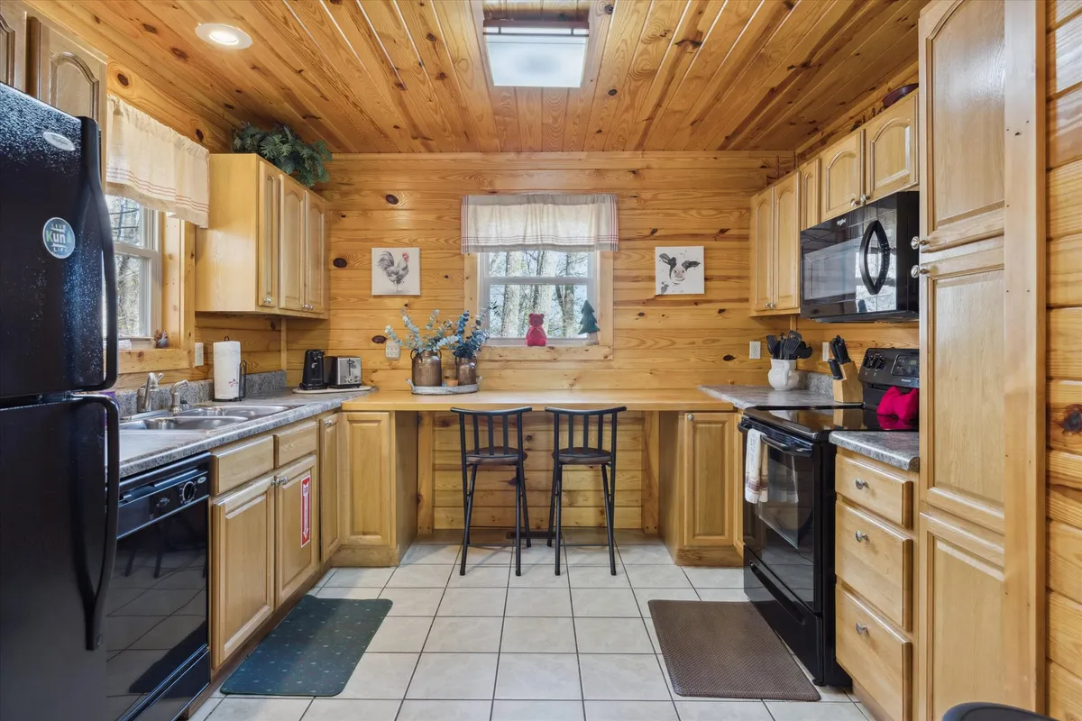 This image captures a spacious kitchen with wooden cabinetry, a central kitchen island with stool seating, and a window adorned with plants that invites natural light. The scene suggests both functionality and warmth, making it ideal for meal prep or enjoying a morning coffee.